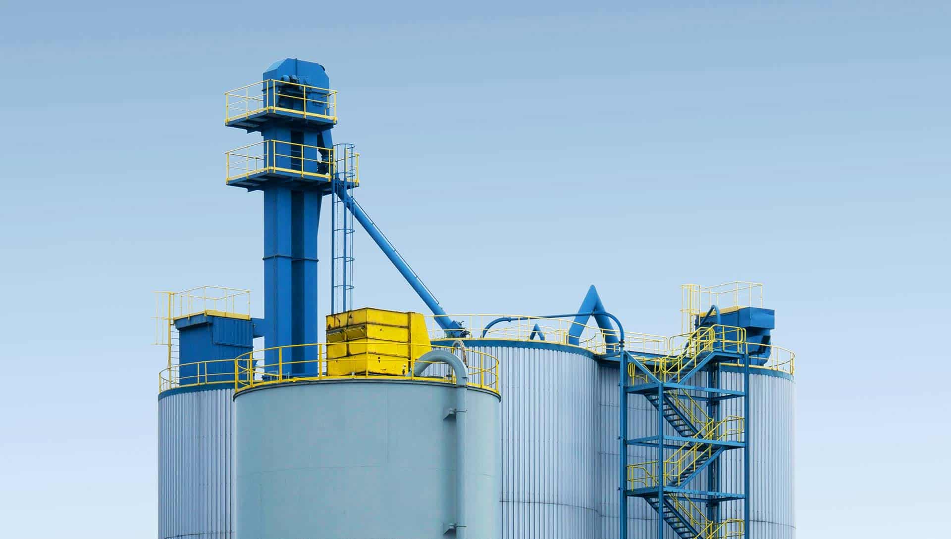 Tanque de acero industrial con sistemas de sinfín y escaleras de acceso, infraestructura para almacenamiento y procesamiento químico.